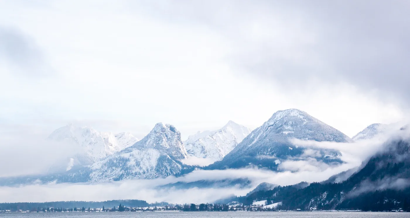 Snow-covered mountains above the Wolfgangsee with low clouds over the lake in winter